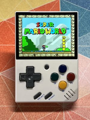 A Miyoo Mini v2 in white. It looks like a miniature Game Boy. The Super Mario World title screen is playing.
