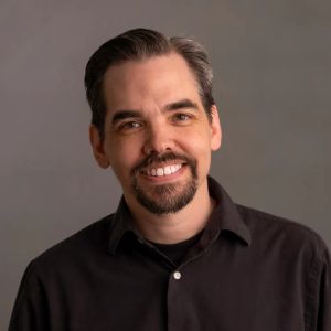Mike, smiling, wearing a black shirt against a gray backdrop.